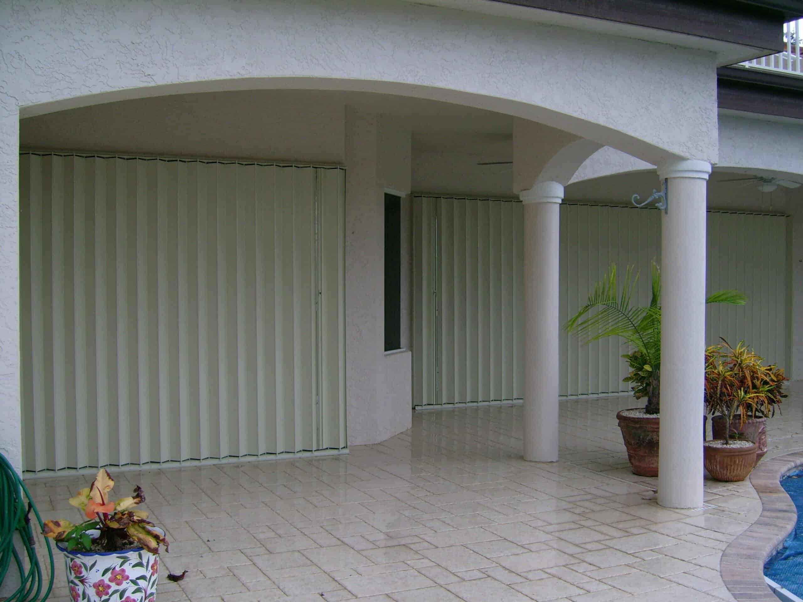 Ivory accordion storm shutters installed on multiple glass sliding doors near a patio