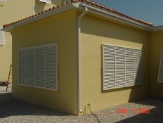 closed white bermuda shutters on yellow house