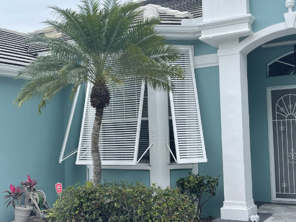 White decorative Bahama hurricane shutters on a teal blue home in Southwest Florida.