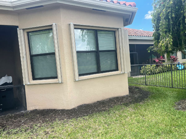 Open, beige accordion shutters shown on windows of a home in Fort Myers