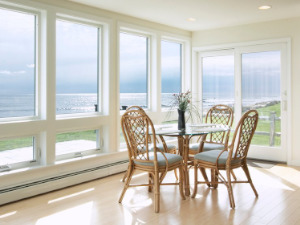 Many white awning impact windows in a light colored dining room with wood floors.