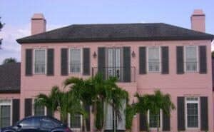 Black colonial hurricane shutters on a pink home