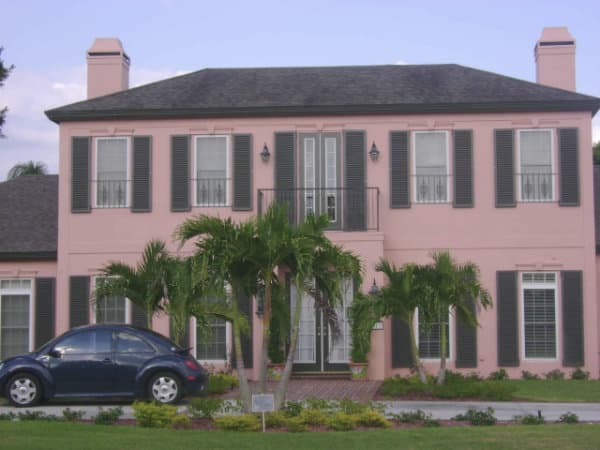 Black Colonial Hurricane Shutters on the front windows and doors of a pink home.