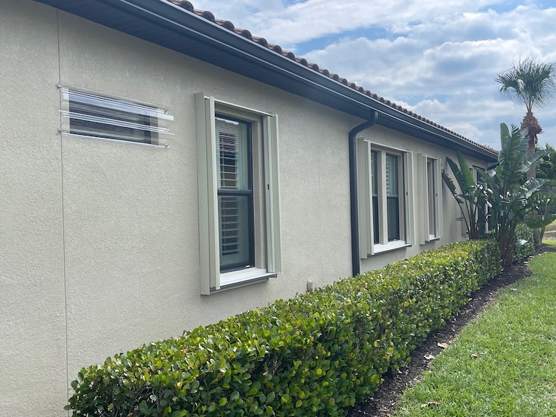 Beige Eurex Shutters PTX Accordions shown on multiple windows along the side of a beige house in the open position.
