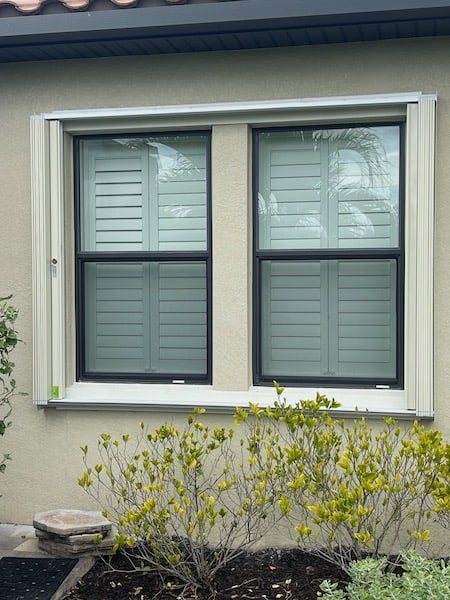 Beige Eurex Shutters PTX Accordion Shutters on medium sized window of a beige house in the open position.