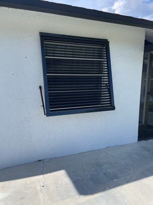 White house with custom, black, full length Bahama shutters to match the black fascia and black trim