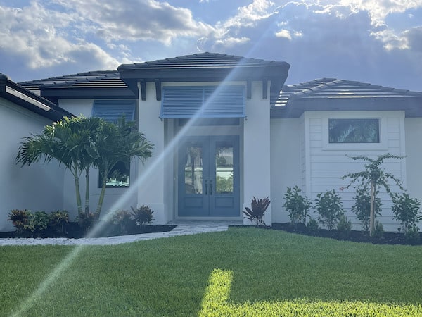 Off white house with blue half-window Bahama hurricane shutters and a blue double entry door