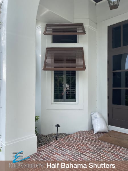 Two half bahama shutters installed on two windows of an off-white stucco home with a dark brown door in Sanibel FL