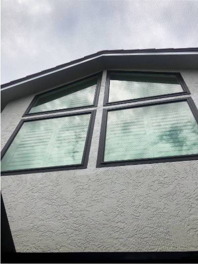 Exterior view of the home. The image shows four custom, impact windows. The two bottom windows are square. The two top windows are trapezoids. All four windows have bronze, aluminum frames. Windows installed on a home in Bonita Springs Florida.