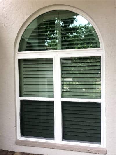 Exterior view of a custom impact window installed by Eurex Shutters in Bonita Springs. There are two side-by-side impact windows with a single impact arch or half-circle window above them. In the view can be seen plantation shutters behind the windows.