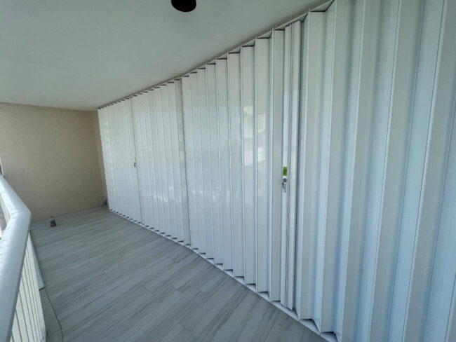 accordion-shutters-condo-marco-island-hoa-1 White Accordion shutters covering the glass of a balcony in Marco Island Florida