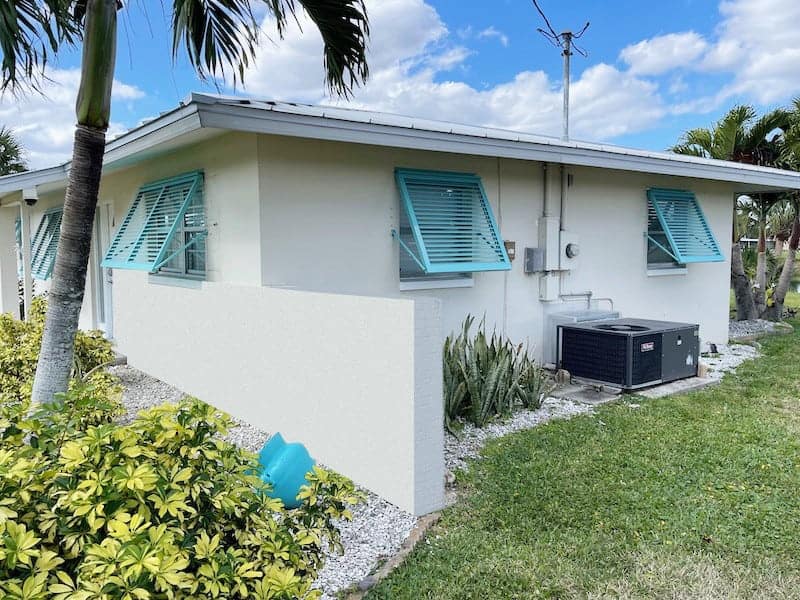 Custom, tiffany blue, Bahama shutters shown installed on the front and right side of a residential home.