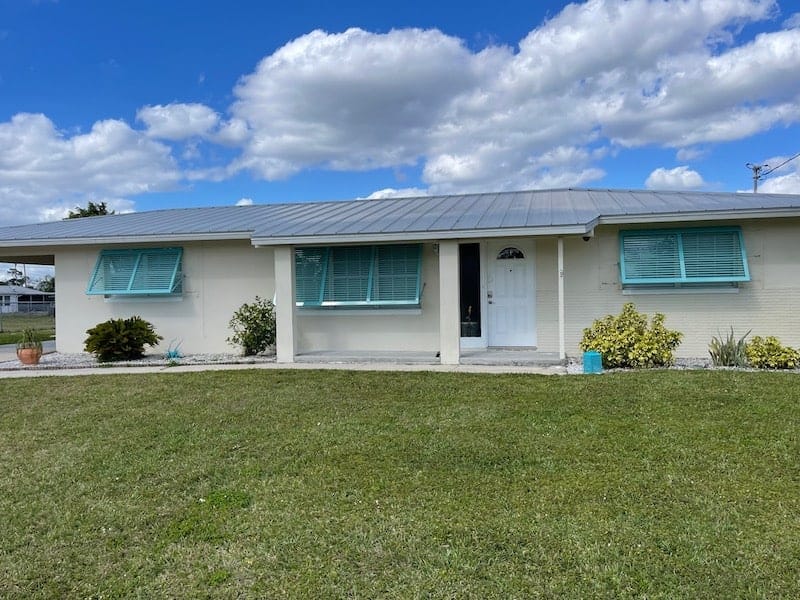 Three wide, custom, blue, full-view, Bahama shutters installed over all the front windows of a Lehigh Acres home.