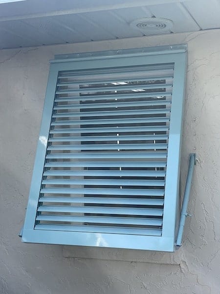 A single, custom, tiffany blue, full view Bahama shutter installed over a small window on the side of a home in Venice Florida.