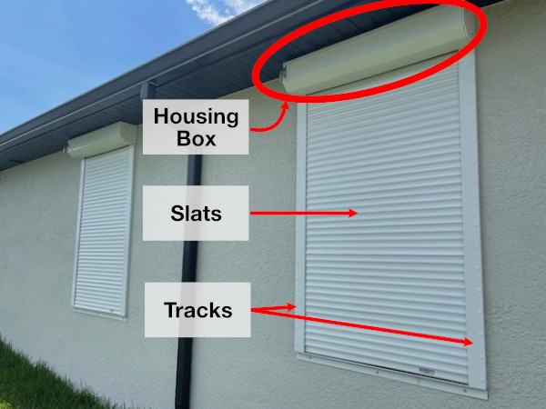 White roll downs shown as a standard installation with housing box visible outside of the home (not hidden). Shows the housing box, slats, and tracks of the shutter installation.
