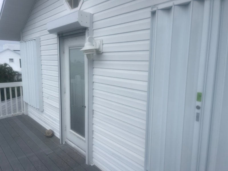 View from the right side of home. White accordion shutters and roll down shutters installed on the doors and windows of a white home in Bokeelia Florida.