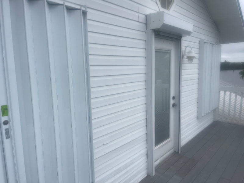 View from the left side of home. White accordion shutters and roll down shutters installed on the doors and windows of a white home in Bokeelia Florida.