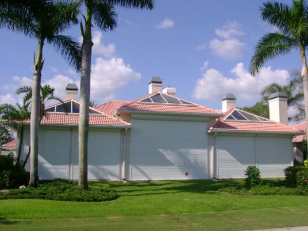 White roll down shutters, a premium type of hurricane shutter, installed on the front of a home with a red tile roof and solar panels.