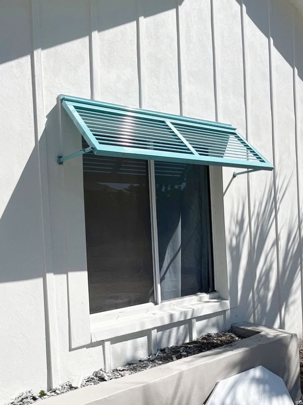 Close-up of a half-Bahama shutter installed over a horizontal roller window of a white, new construction home on Sanibel.