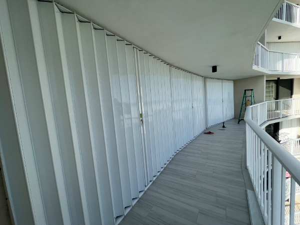 White accordion shutters installed along the width of a condo balcony in Marco Island Florida.
