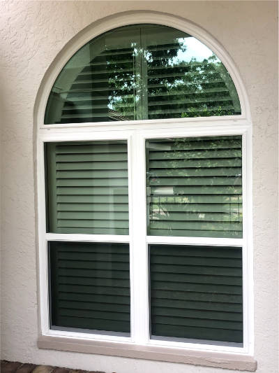 White, custom impact windows and arch (half-circle windows) installed on a beige home in Bonita Springs