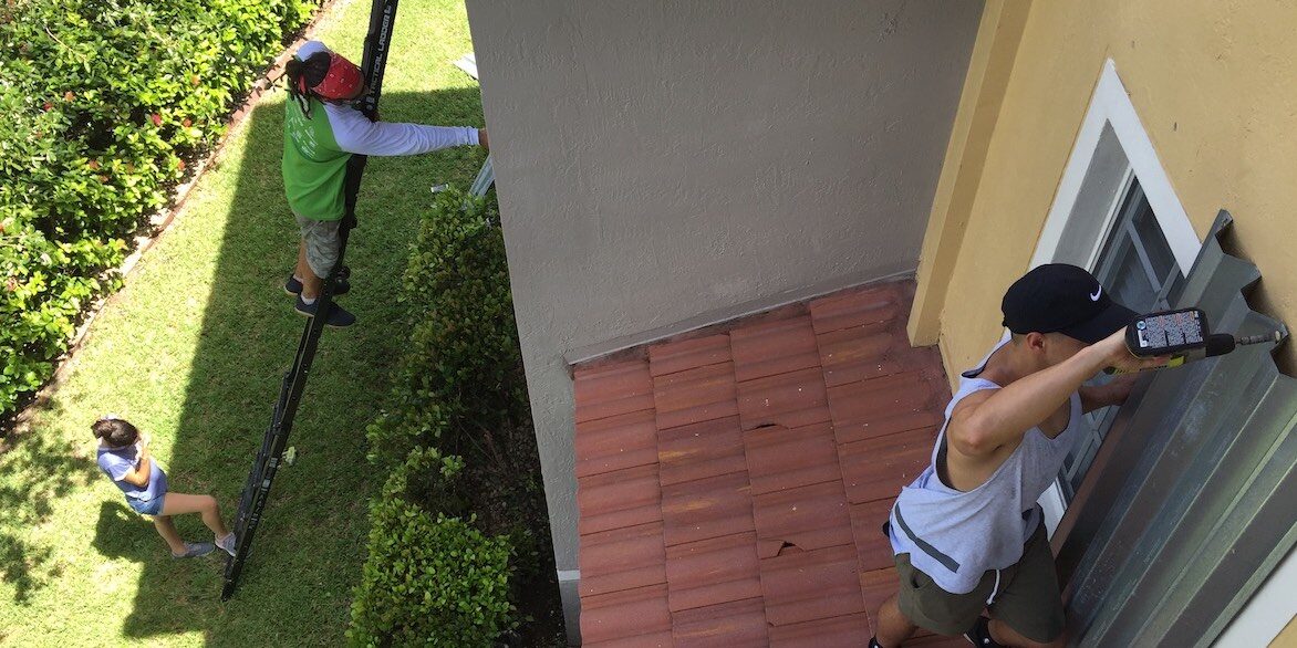 Hurricane-preparations-second-floor person installing hurricane shutters on second floor on ladder