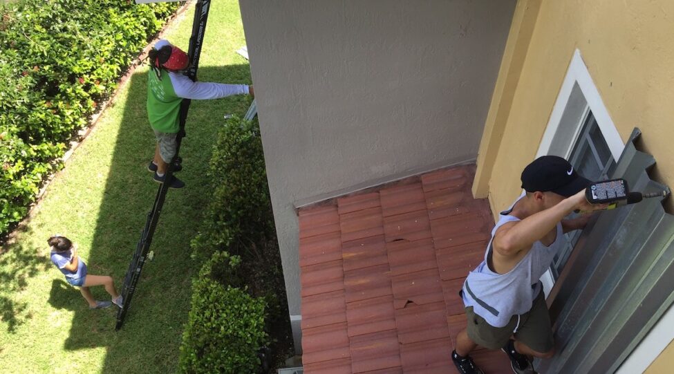 Hurricane-preparations-second-floor person installing hurricane shutters on second floor on ladder