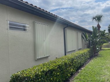 Beige accordion shutters closed over windows on a home