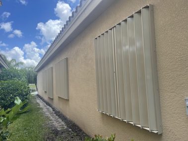 Beige accordion shutters closed over windows on a home