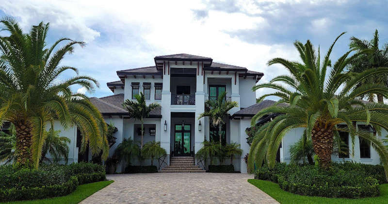 A British West-Indies style home with lush landscaping and palm trees.