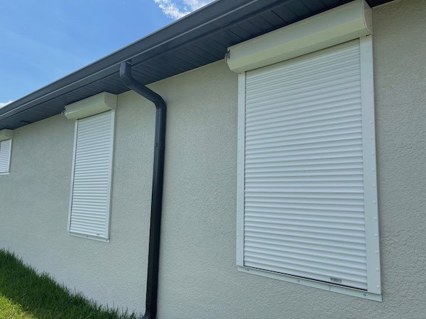 Tan roll-down shutters shown on a beige home.