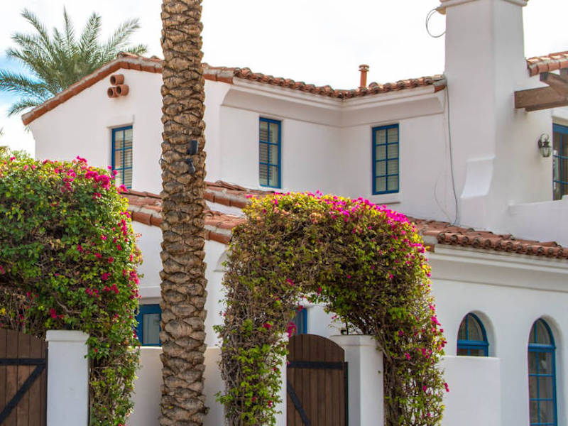 A white Mediterranean style home with arched entry, arched windows, and red tile roof.
