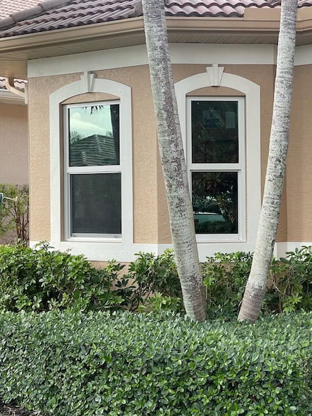 House in Naples, Florida, with a tree in front, showcasing newly installed impact windows by Eurex Shutters.