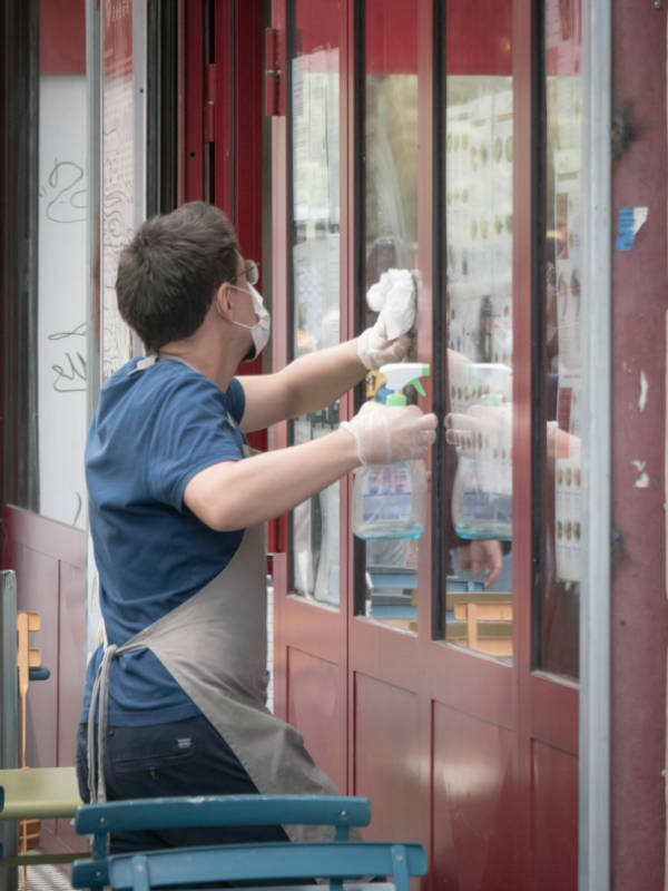 Man with a blue shirt and gloves cleaning exterior windows with cleaning fluid and a cloth.