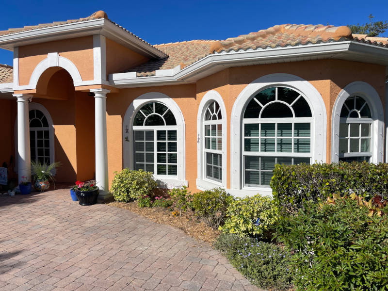 Arched, impact windows with grilles on an orange, Mediterranean style home with white trim and a terracotta tile roof.